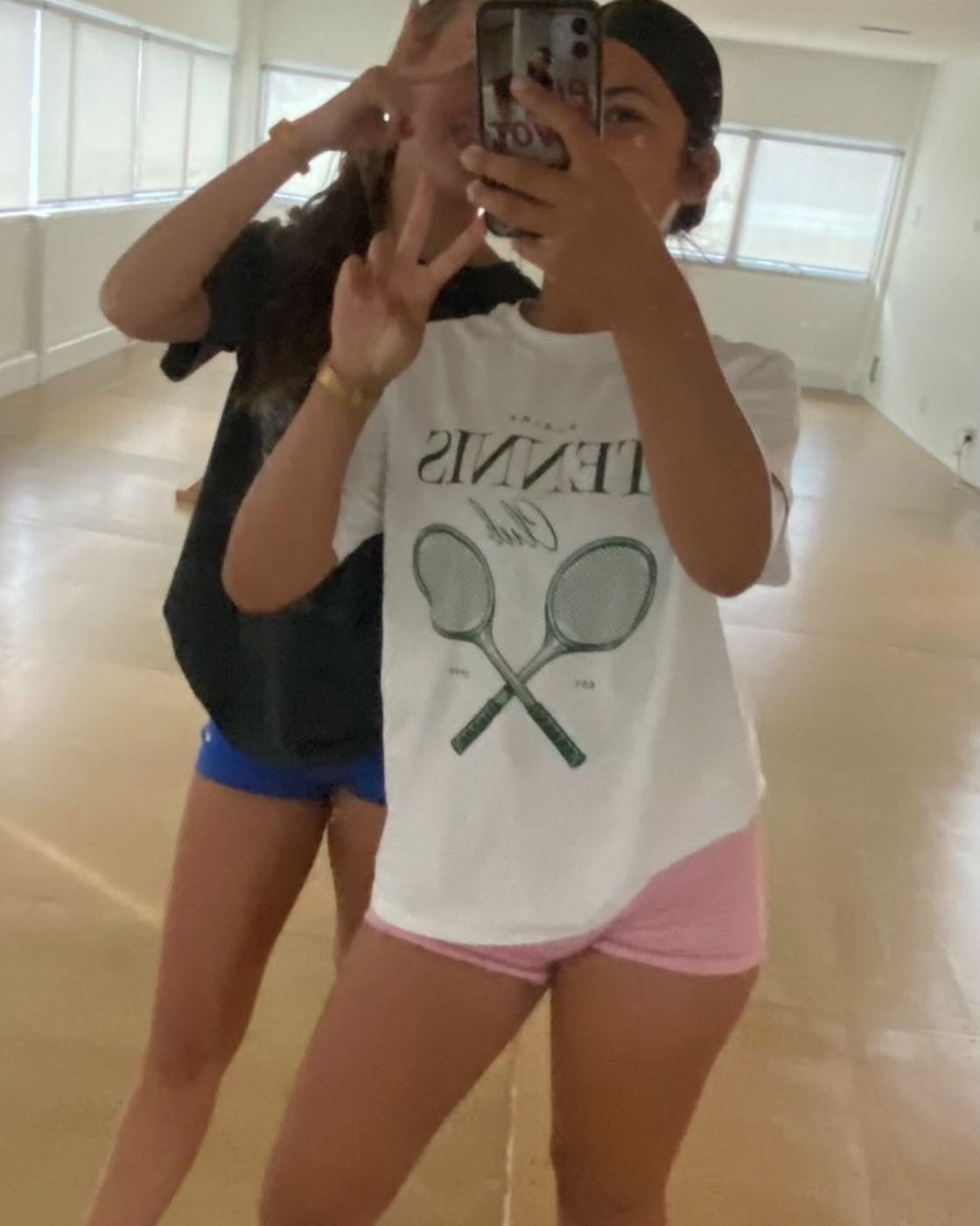 Customer taking a mirror selfie in the Blaire Tennis Club Tee, styled with gym shorts and trainers